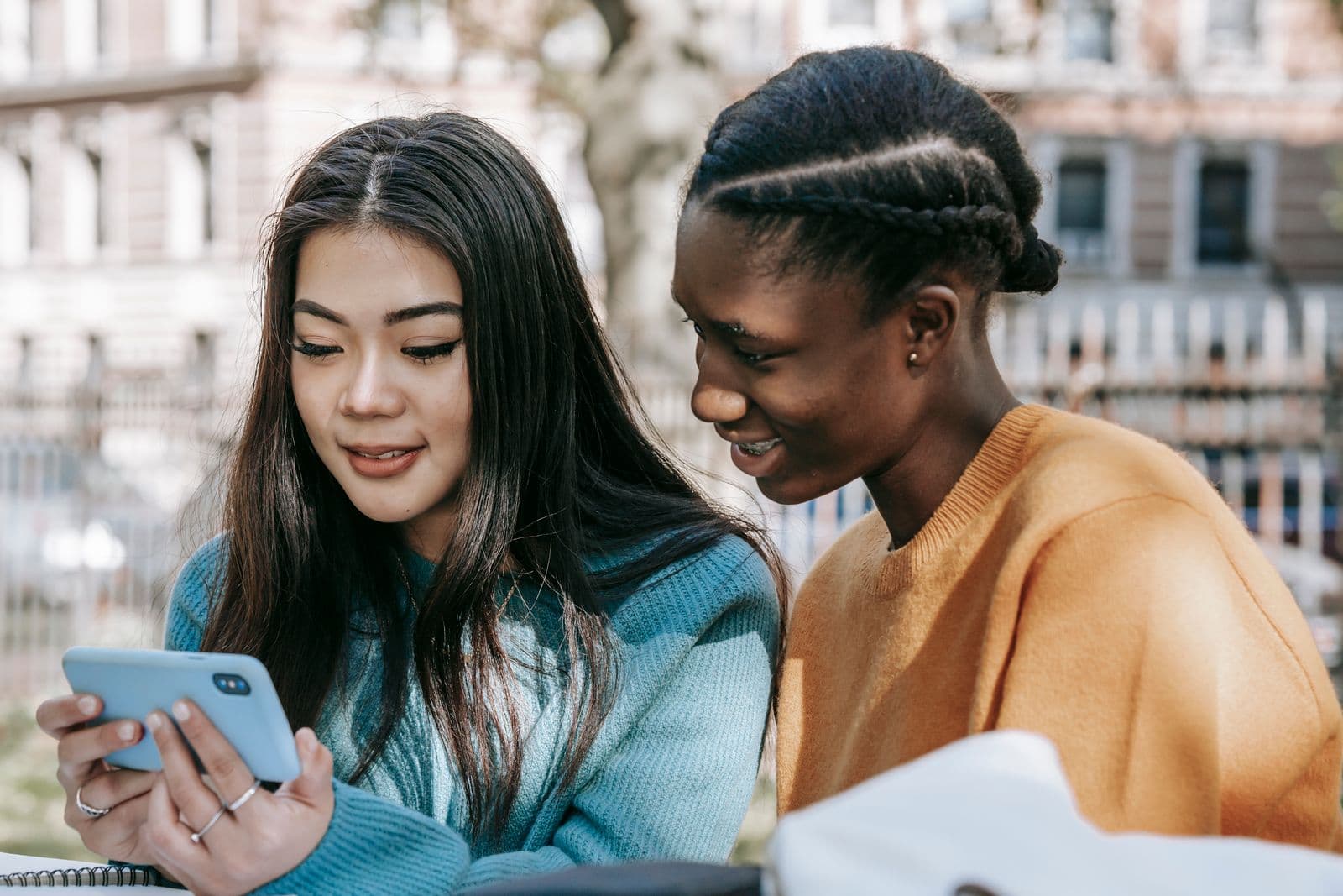 Two friends smiling at a phone together outdoors