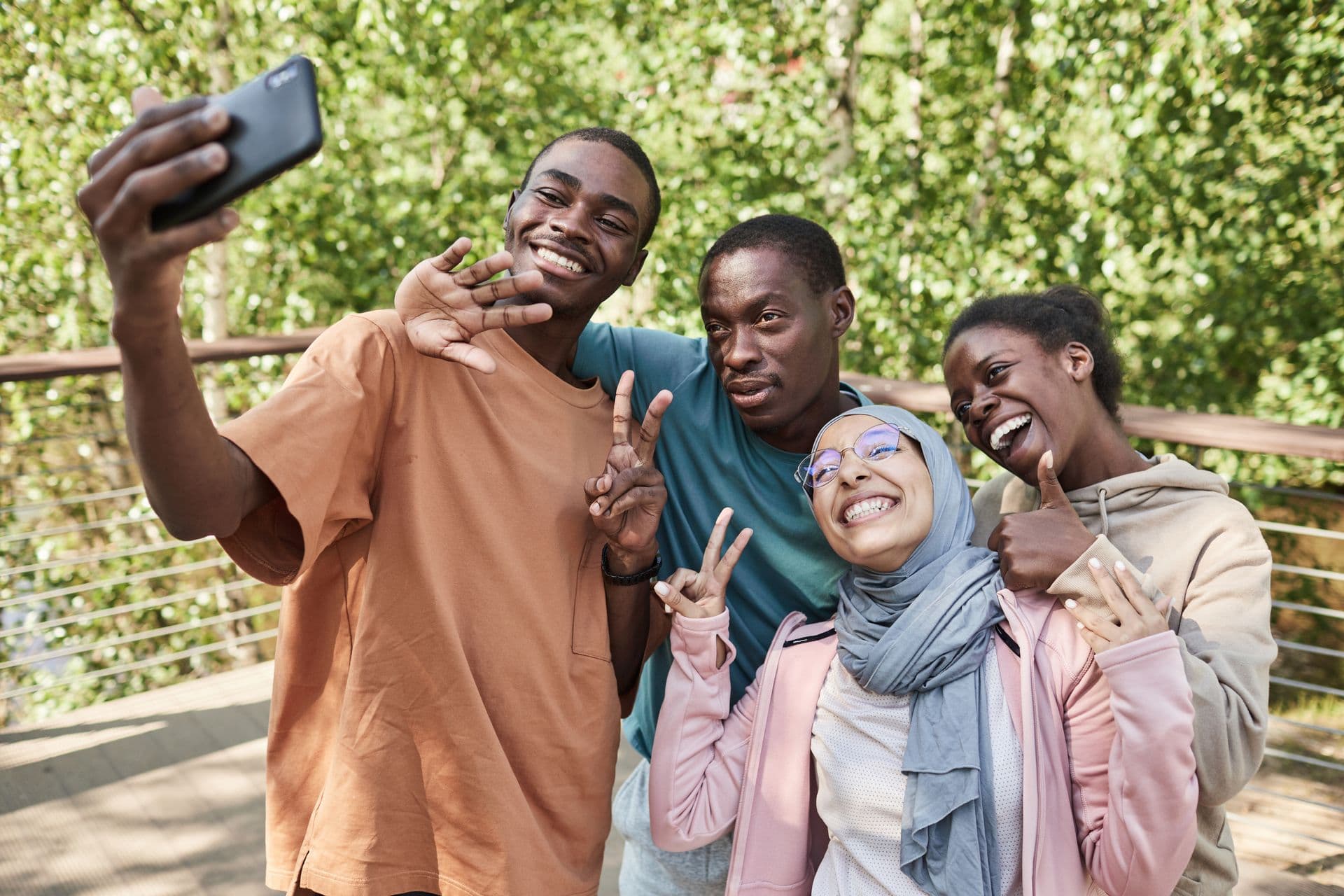 Four friends laughing together while taking a selfie in a sunny park